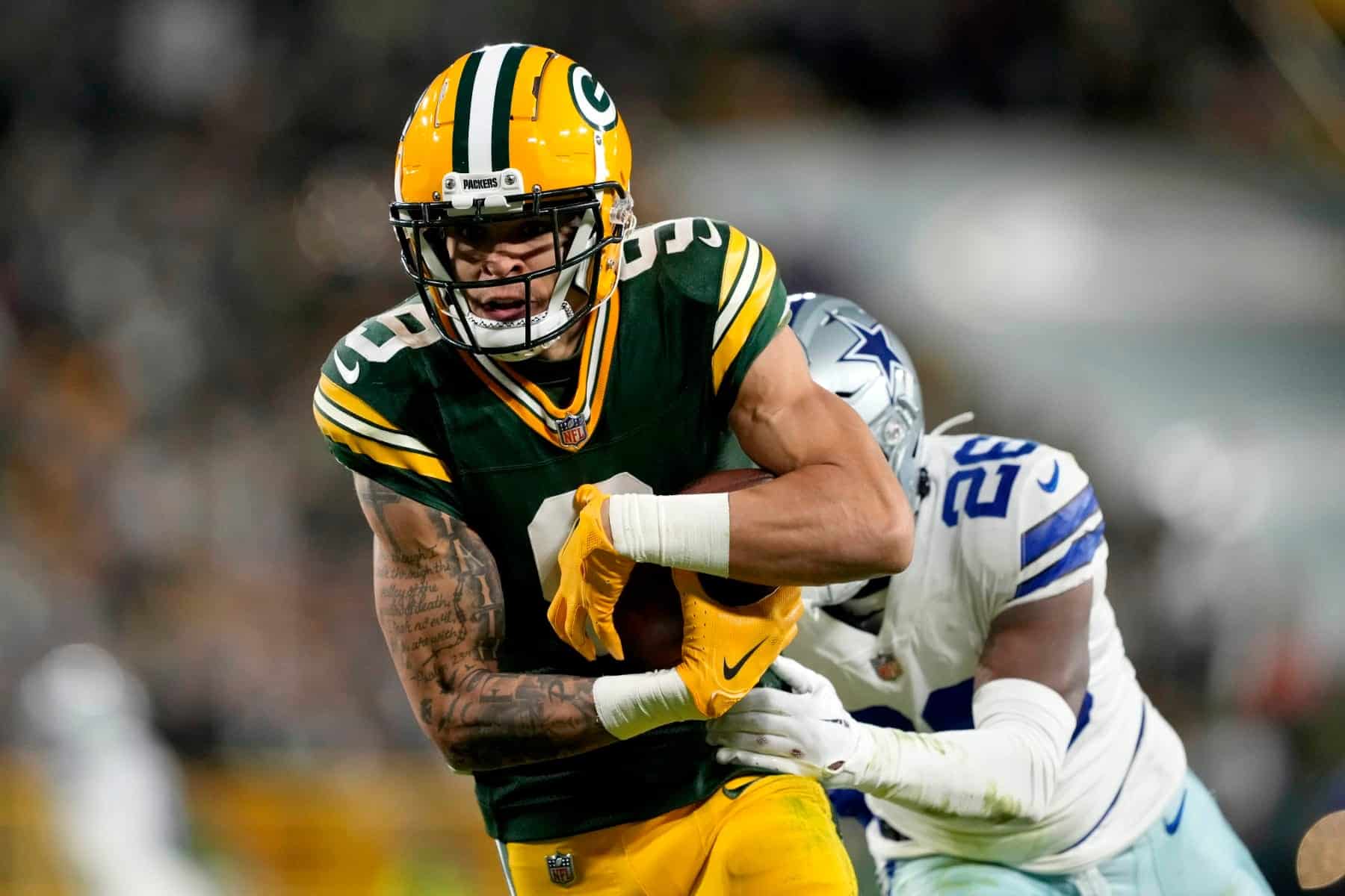 Green Bay Packers player running with football during game against Dallas Cowboys, defensive player attempting to tackle, NFL football action, inside football stadium, team uniforms.