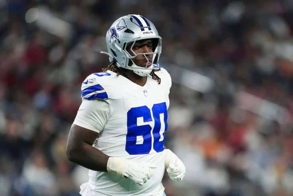 Dallas Cowboys football player in full gear on the field, wearing number 60, during an NFL game. The player is focused and ready for action, showcasing team pride and athleticism.