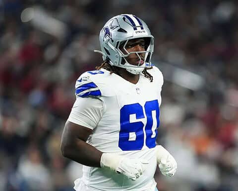 Dallas Cowboys football player in full gear on the field, wearing number 60, during an NFL game. The player is focused and ready for action, showcasing team pride and athleticism.