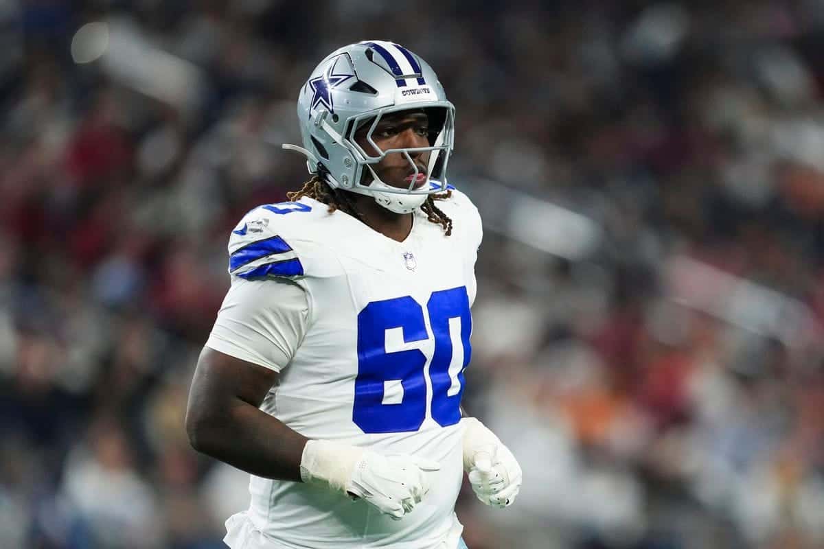 Dallas Cowboys football player in full gear on the field, wearing number 60, during an NFL game. The player is focused and ready for action, showcasing team pride and athleticism.