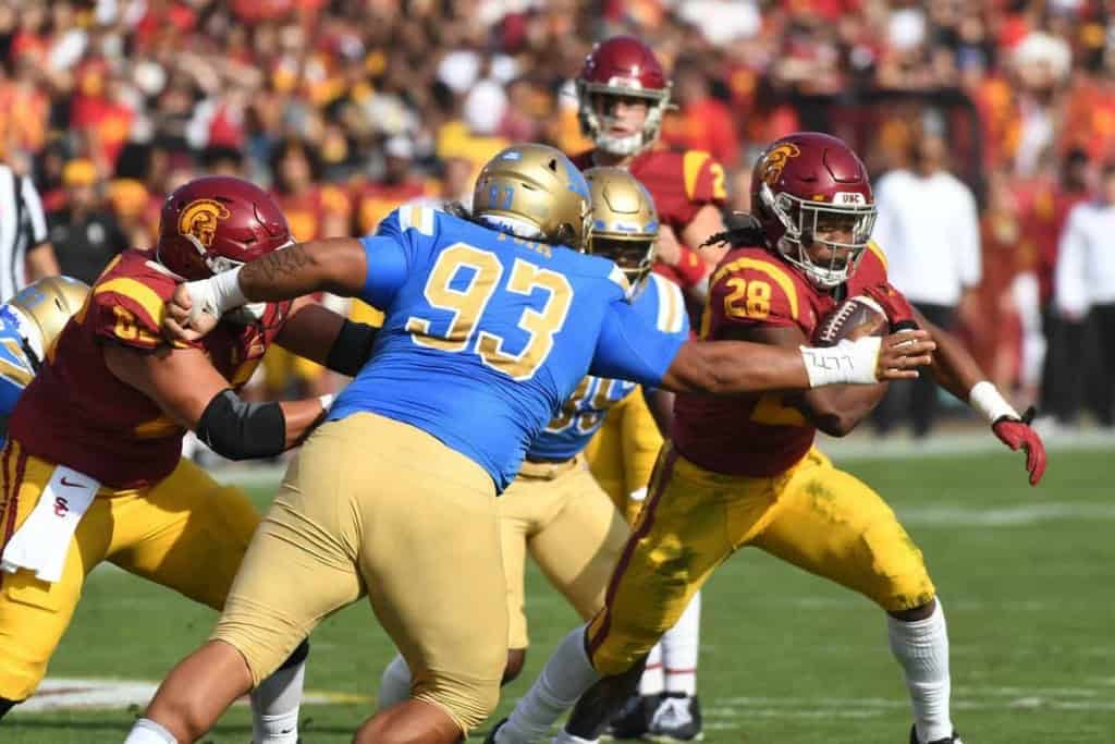 USC Trojans football player running with the ball against UCLA Bruins defenders during a game at the stadium.
