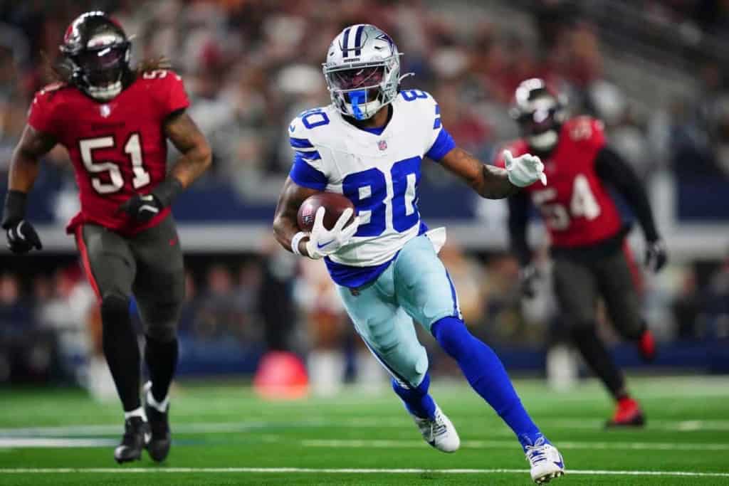 Speeding NFL athlete in Dallas Cowboys uniform running with football on the field during game action.
