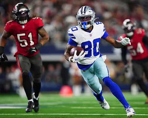 Speeding NFL athlete in Dallas Cowboys uniform running with football on the field during game action.