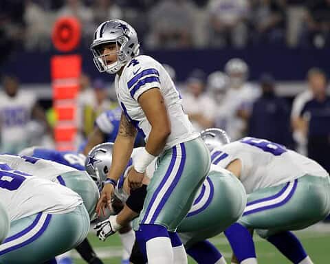 Dallas Cowboys football quarterback preparing to throw, standing behind offensive line during game.