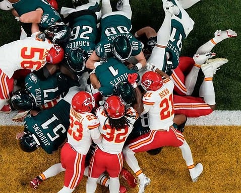 Aerial view of an intense NFL football game with players from the Kansas City Chiefs and Philadelphia Eagles engaged in a tackle play on the field.