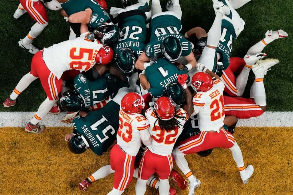 Aerial view of an intense NFL football game with players from the Kansas City Chiefs and Philadelphia Eagles engaged in a tackle play on the field.