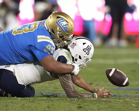 UCLA football player tackled during game on the field, football in mid-air, showcasing intense action and athleticism, Inside The Star sports coverage.