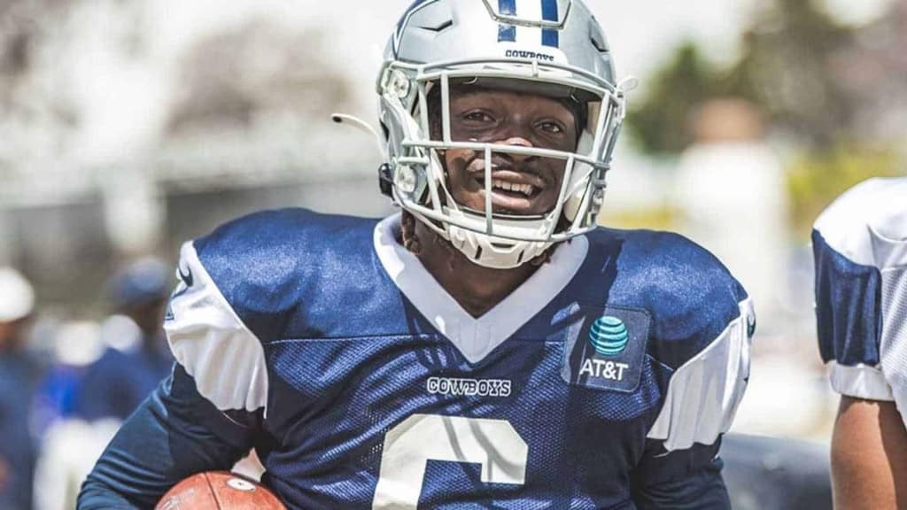 Aggressive Dallas Cowboys football player in action, wearing helmet and uniform, holding football, demonstrating strength, speed, and team pride, on a sunny day at the field.