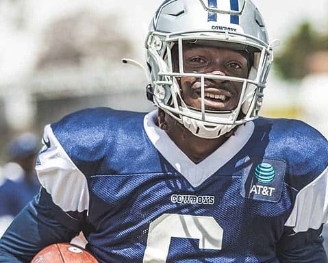 Aggressive Dallas Cowboys football player in action, wearing helmet and uniform, holding football, demonstrating strength, speed, and team pride, on a sunny day at the field.