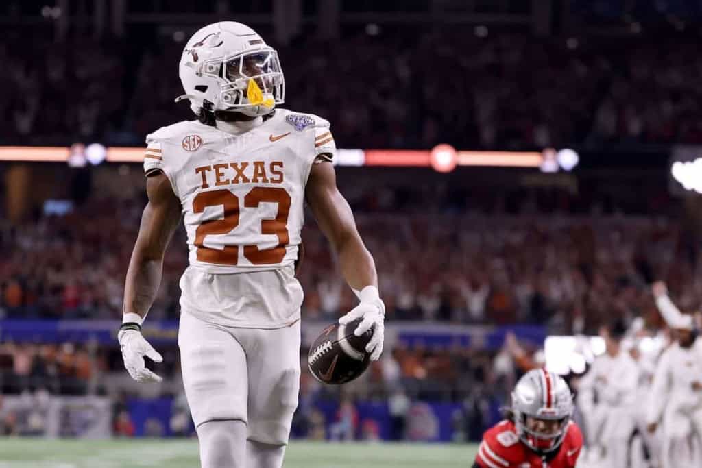 Athletic football player from Texas Longhorns holding a football during a game, wearing white jersey with the number 23, in a stadium filled with fans.