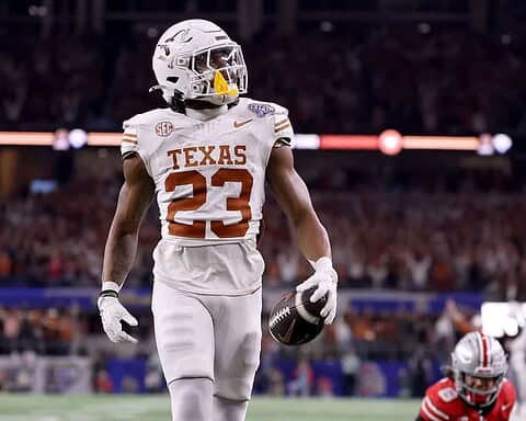 Athletic football player from Texas Longhorns holding a football during a game, wearing white jersey with the number 23, in a stadium filled with fans.