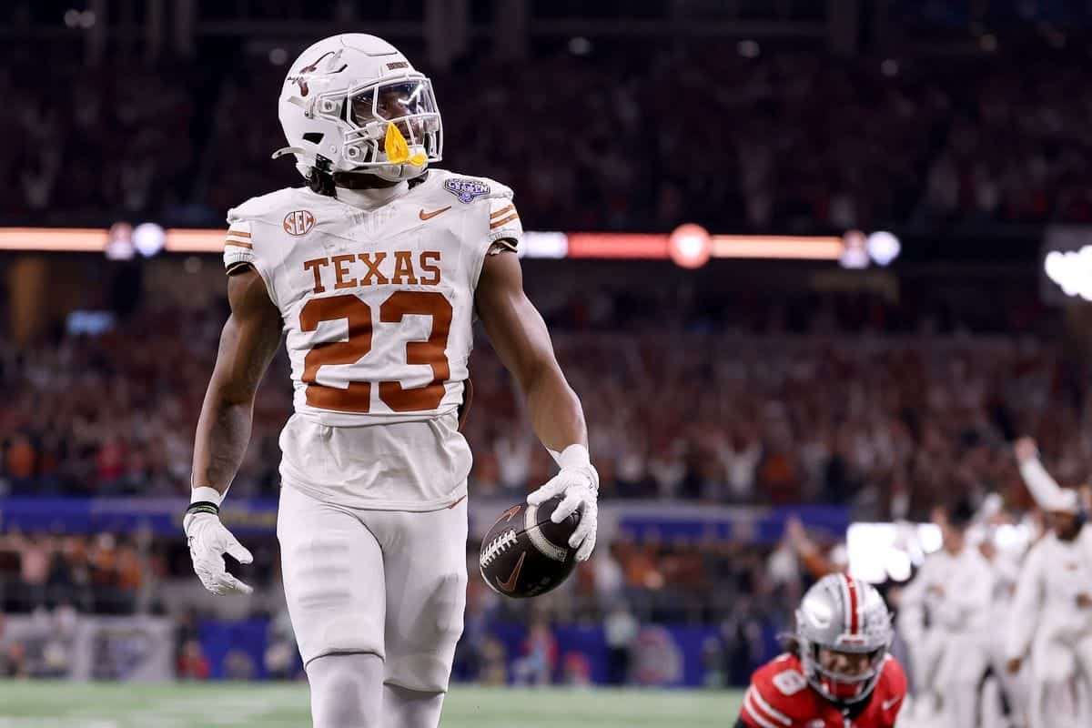 Athletic football player from Texas Longhorns holding a football during a game, wearing white jersey with the number 23, in a stadium filled with fans.