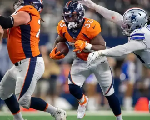 Broncos football player in orange uniform running with ball during game against Cowboys Dallas team.