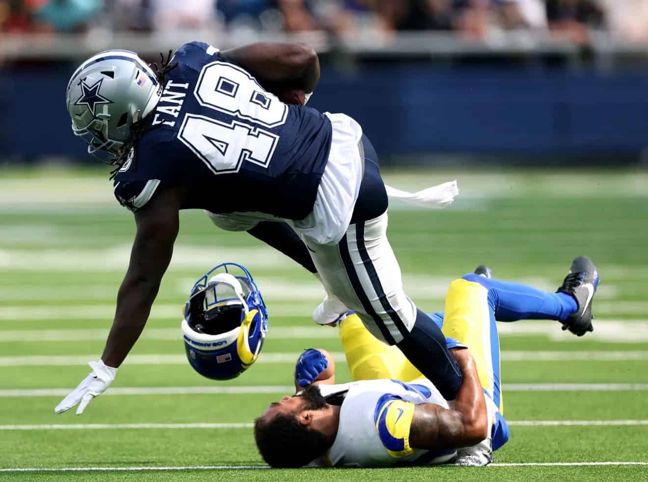 Aggressive football player in Dallas Cowboys uniform making a tackle on opponent during a game, showcasing NFL action, sports competition, and athletic effort.