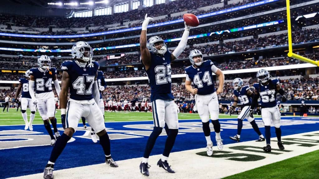 Dallas Cowboys football players celebrating touchdown at AT&T Stadium during NFL game, team in navy and white uniforms, stadium filled with fans, bright lights, action-packed moment.