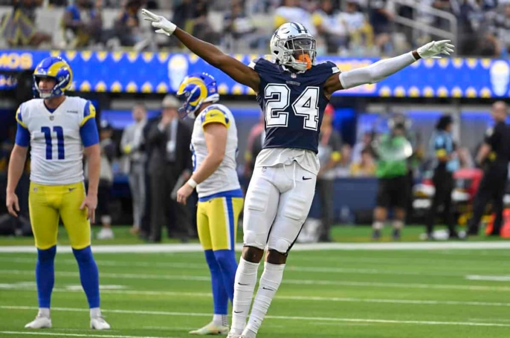 Athletic football player celebrating on field during game, wearing jersey number 24, with teammates in the background, emphasizing NFL sports action and team spirit.
