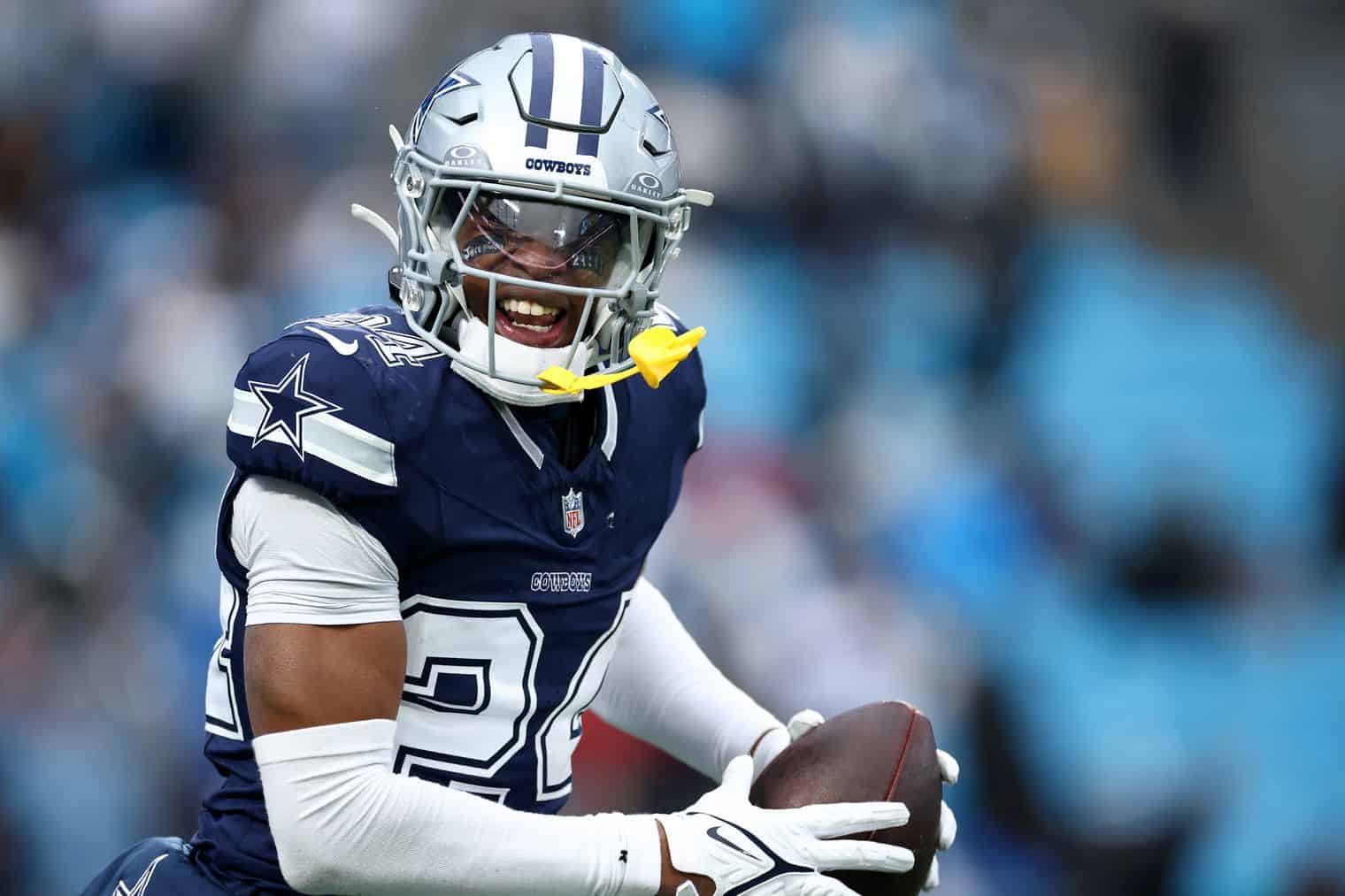 Dallas Cowboys football player running with the ball during a game, wearing team uniform, helmet, and safety gear, showcasing athleticism and team spirit, inside the NFL stadium.