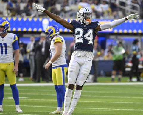 Athletic football player celebrating on field during game, wearing jersey number 24, with teammates in the background, emphasizing NFL sports action and team spirit.