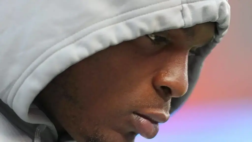 Close-up of a young athlete wearing a gray hoodie, focused and reflective, likely during a training session or game, showcasing determination and concentration in American football or sports performance.
