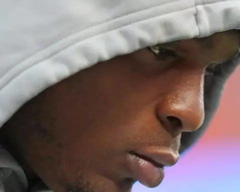 Close-up of a young athlete wearing a gray hoodie, focused and reflective, likely during a training session or game, showcasing determination and concentration in American football or sports performance.