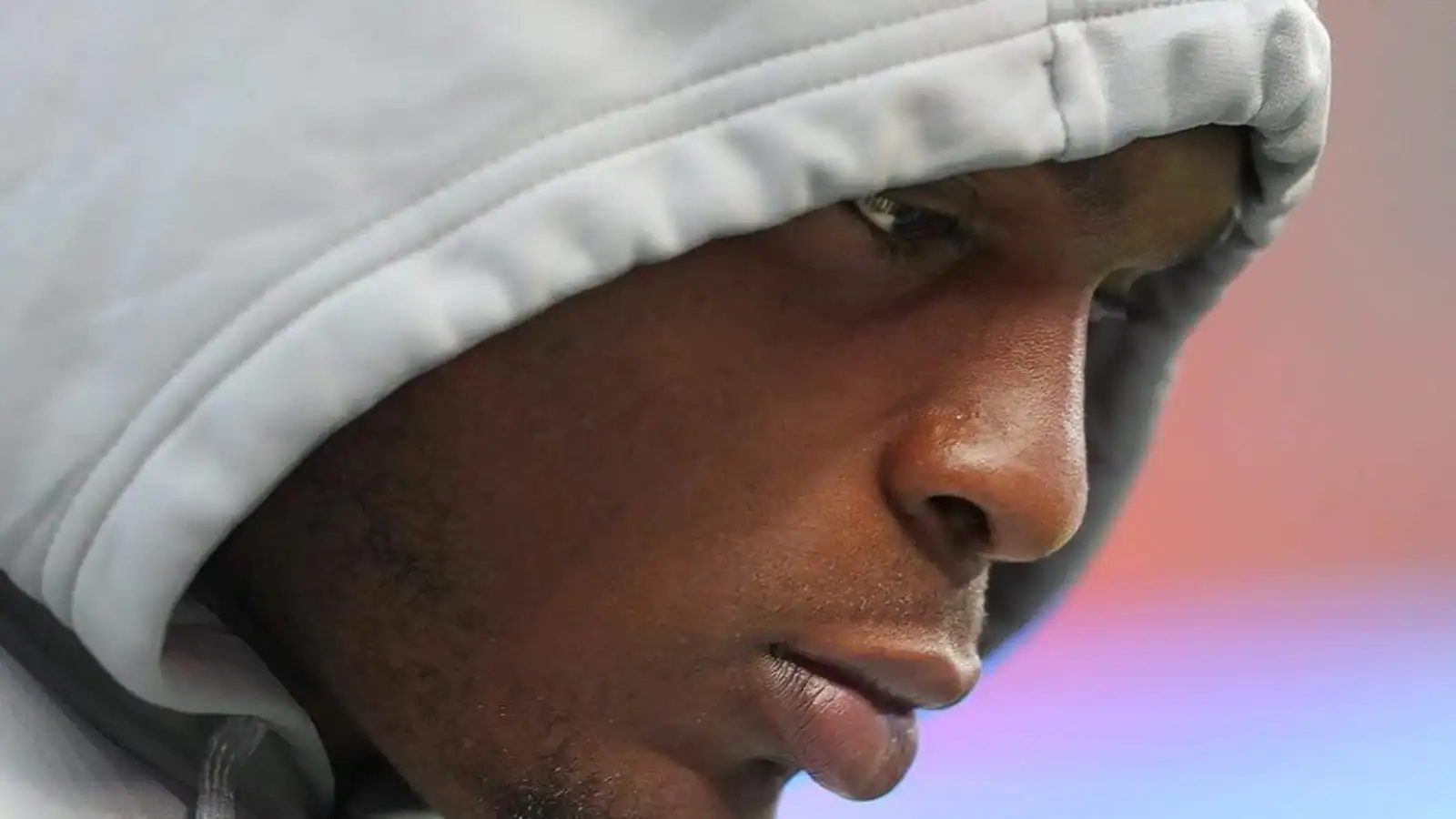 Close-up of a young athlete wearing a gray hoodie, focused and reflective, likely during a training session or game, showcasing determination and concentration in American football or sports performance.