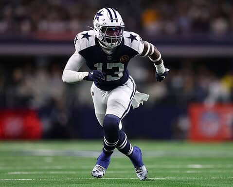 Dallas Cowboys football player running on the field during a game, wearing team uniform and helmet.