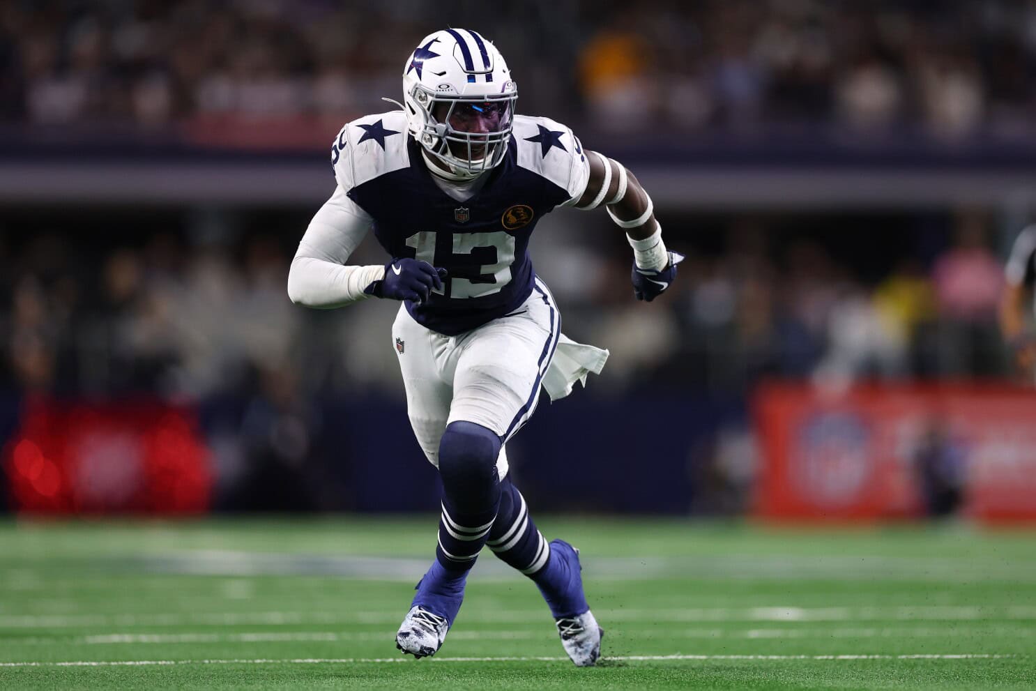 Dallas Cowboys football player running on the field during a game, wearing team uniform and helmet.