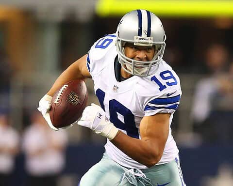 Aggressive Dallas Cowboys football player running with football during game, wearing helmet and uniform, focused on advancing on the field.