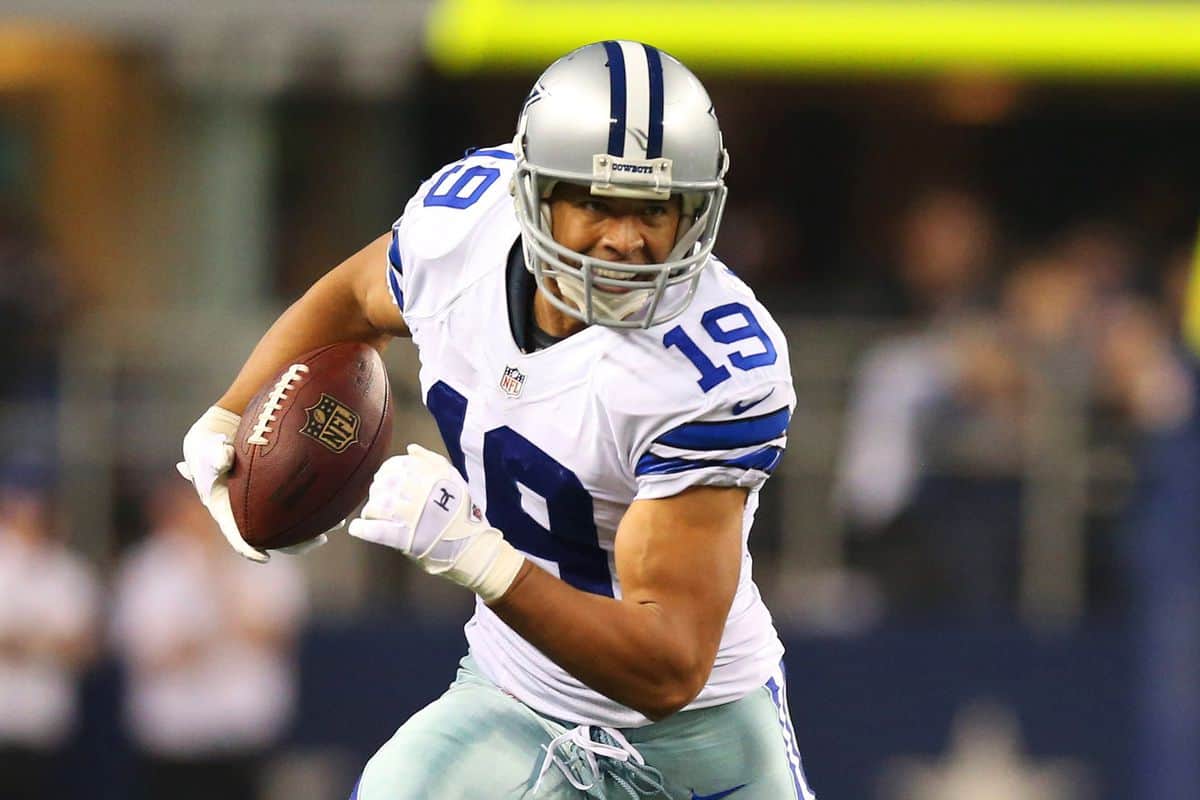 Aggressive Dallas Cowboys football player running with football during game, wearing helmet and uniform, focused on advancing on the field.