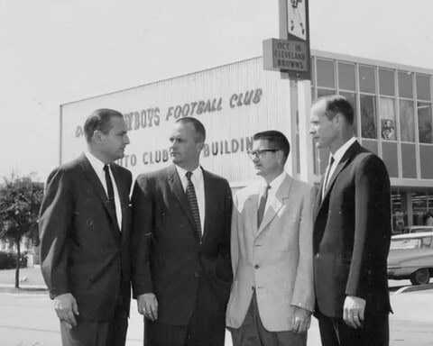 Men in suits standing outside Dallas Cowboys Football Club building, vintage black-and-white photo.