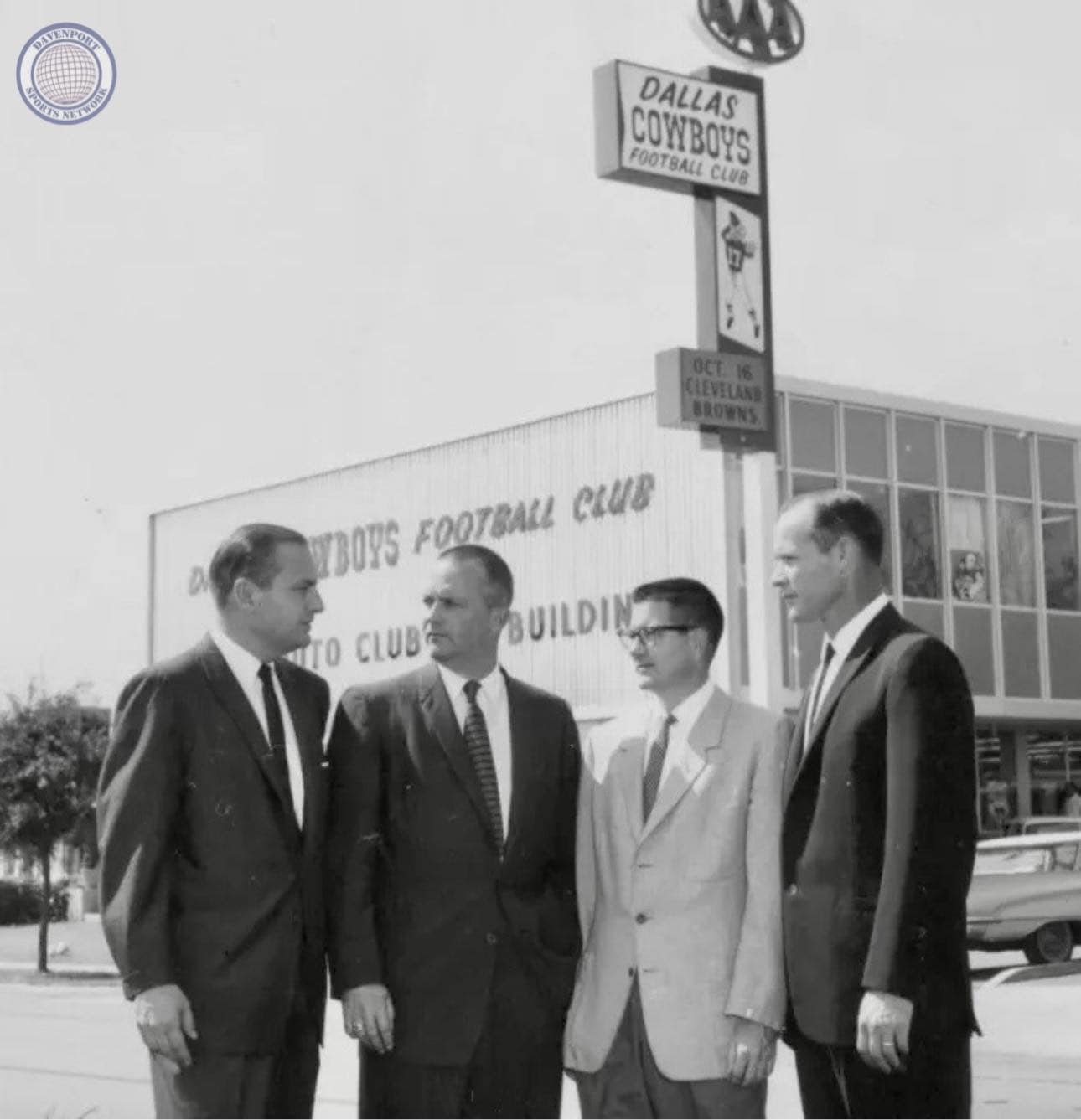 Men in suits standing outside Dallas Cowboys Football Club building, vintage black-and-white photo.