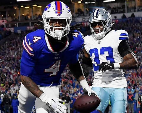 Eyebrow-raising NFL football game featuring Buffalo Bills player in blue jersey with number 4 catching a touchdown pass, and Dallas Cowboys player in white jersey with number 13 in close defense during a packed stadium.
