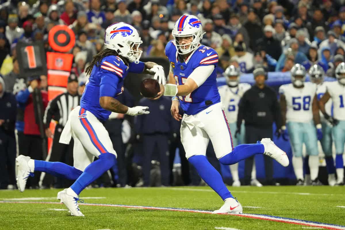 Dynamic football players from the Buffalo Bills in action during an NFL game, with one player handing off the football to a teammate on the field, surrounded by an engaged crowd and team members in the background.