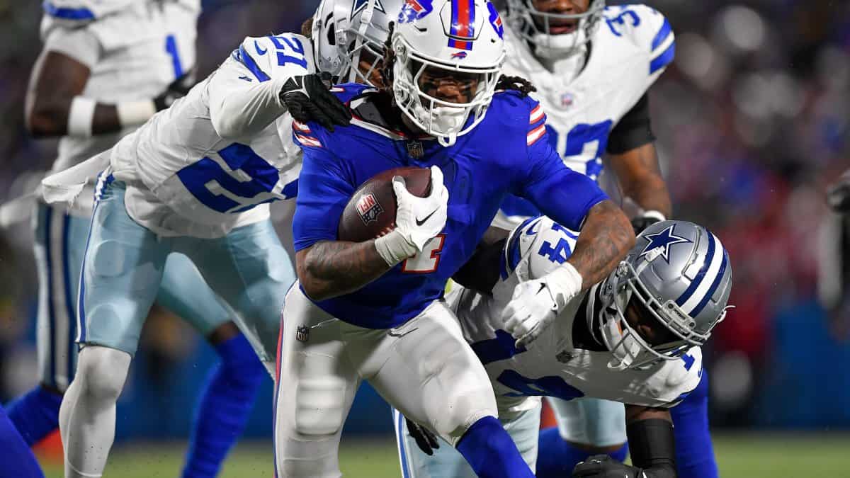 - Running back in blue jersey holding football, tackled by Dallas Cowboys defenders during NFL game.