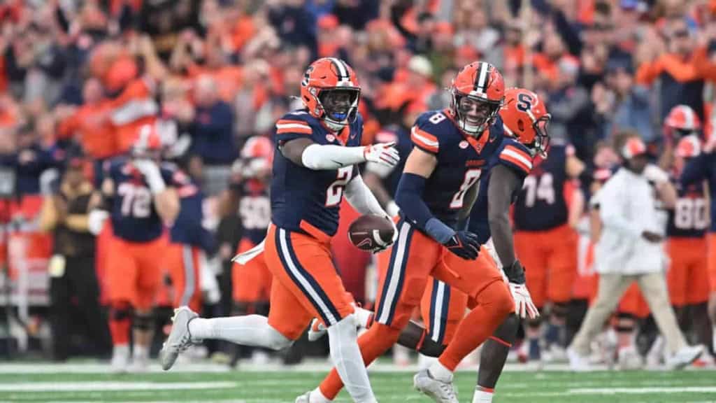 Young football players celebrating on the field during a game, wearing orange and navy uniforms, representing the Dallas Cowboys, inside the star, NFL football, sports action, team victory.