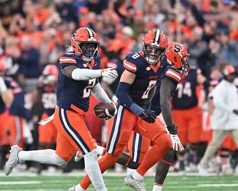 Young football players celebrating on the field during a game, wearing orange and navy uniforms, representing the Dallas Cowboys, inside the star, NFL football, sports action, team victory.
