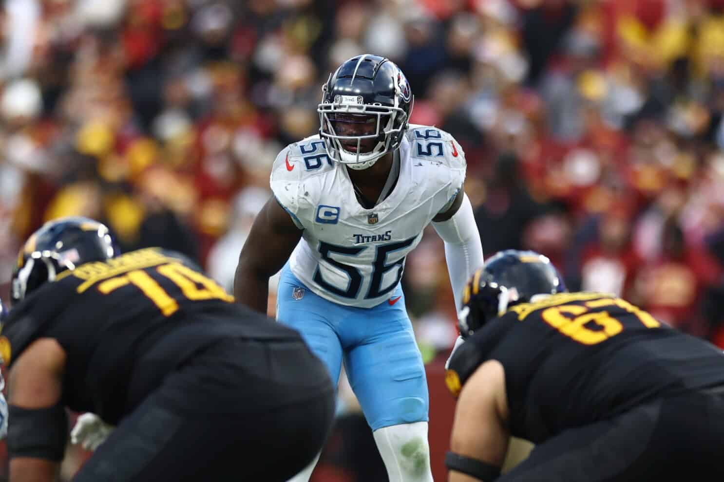 High school football players during a game, featuring a player from the Tennessee Titans in a defensive stance, with opposing team players in black uniforms, showcasing intense action on the field.
