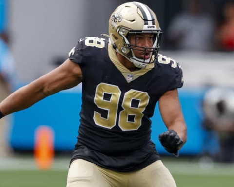 Aggressive football player in black and gold New Orleans Saints jersey number 98 during game action, on the field with blurred stadium background.