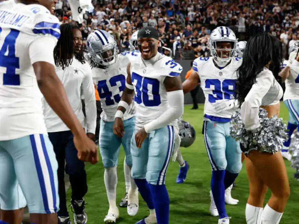 Celebrating Dallas Cowboys football players on the field during a game, showcasing team spirit, camaraderie, and excitement with players in uniforms, including wide receivers and cheerleaders.