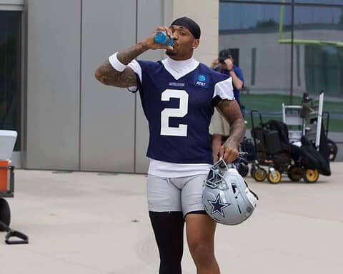 Athlete drinking water wearing Dallas Cowboys football uniform at practice or game day, holding helmet, NFL player, sports, football training, inside the star.
