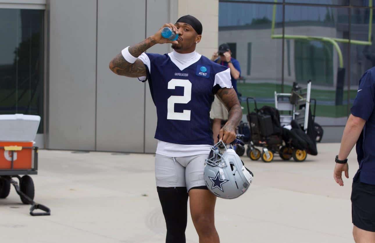 Athlete drinking water wearing Dallas Cowboys football uniform at practice or game day, holding helmet, NFL player, sports, football training, inside the star.