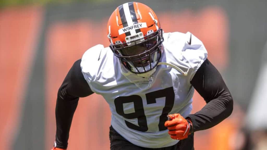 High school football player in action during practice, wearing a white jersey with the number 97, an orange helmet with black and white stripes, and black sleeves.