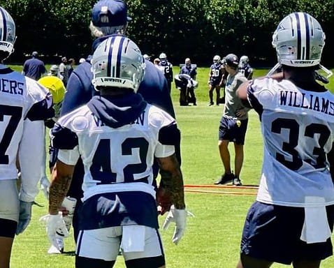 High school football players wearing Dallas Cowboys jerseys during practice or game on a sunny day, with coaches and players in the background.