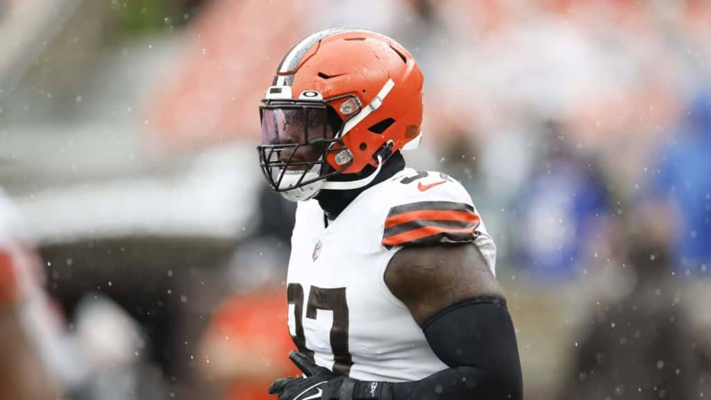 Football player wearing orange helmet and white jersey with black and orange accents, on the field in rainy weather.