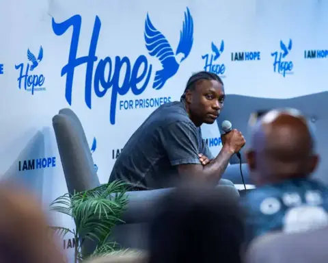 A man speaking into a microphone at the Inside The Star event, with a backdrop featuring Hope for Prisoners and Dallas Cowboys logos, promoting hope and rehabilitation for prisoners.
