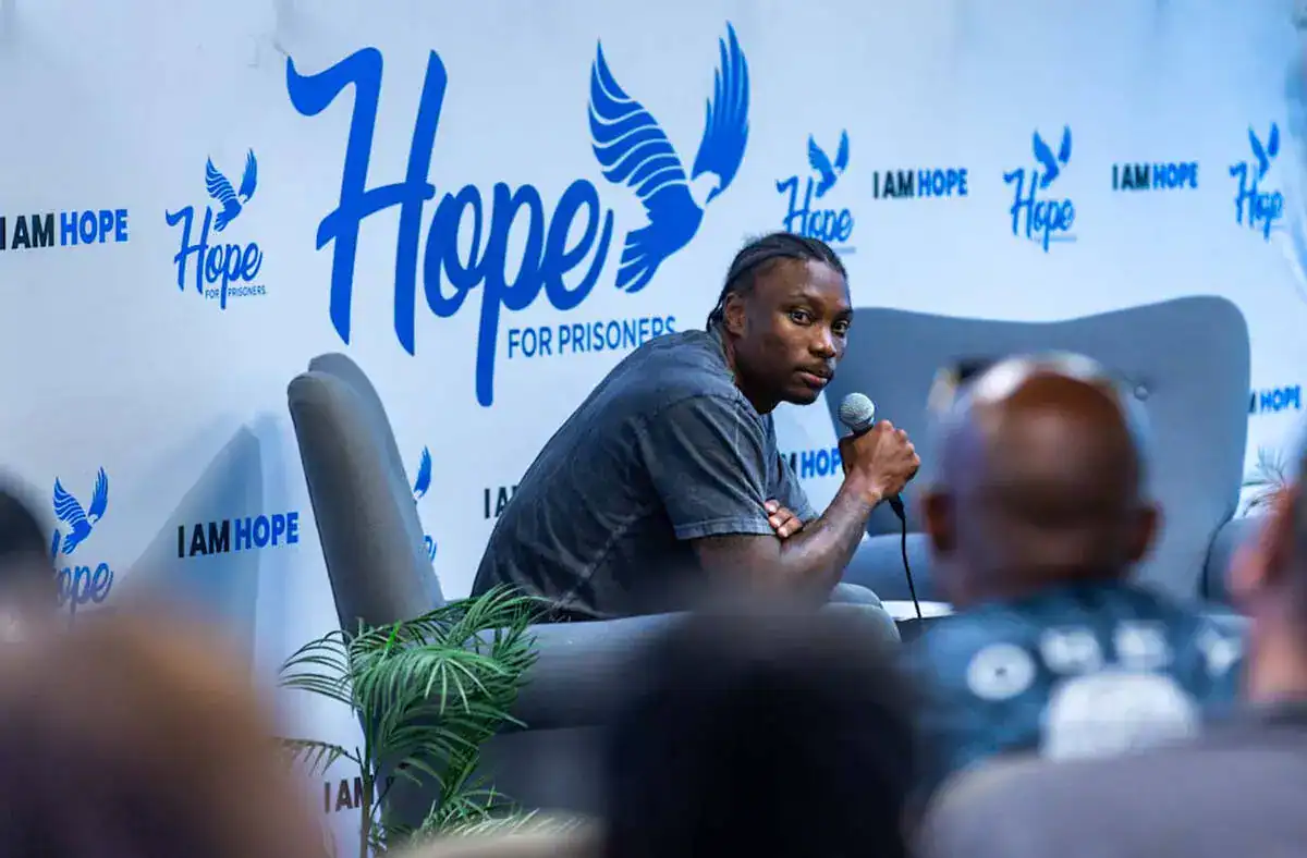 A man speaking into a microphone at the Inside The Star event, with a backdrop featuring Hope for Prisoners and Dallas Cowboys logos, promoting hope and rehabilitation for prisoners.