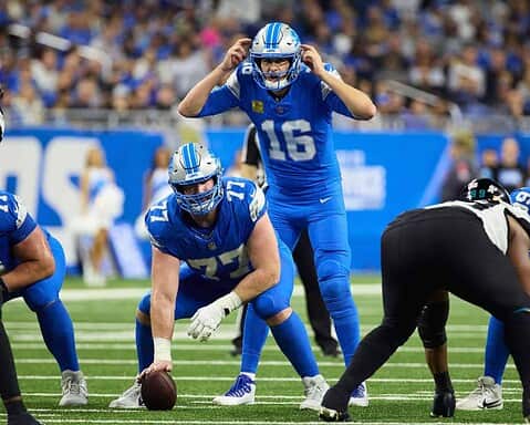 Downtown Detroit Lions quarterback scrambling during an NFL game against the Jacksonville Jaguars. Photo captures action on the field with players in blue uniforms, highlighting the intensity of professional football.