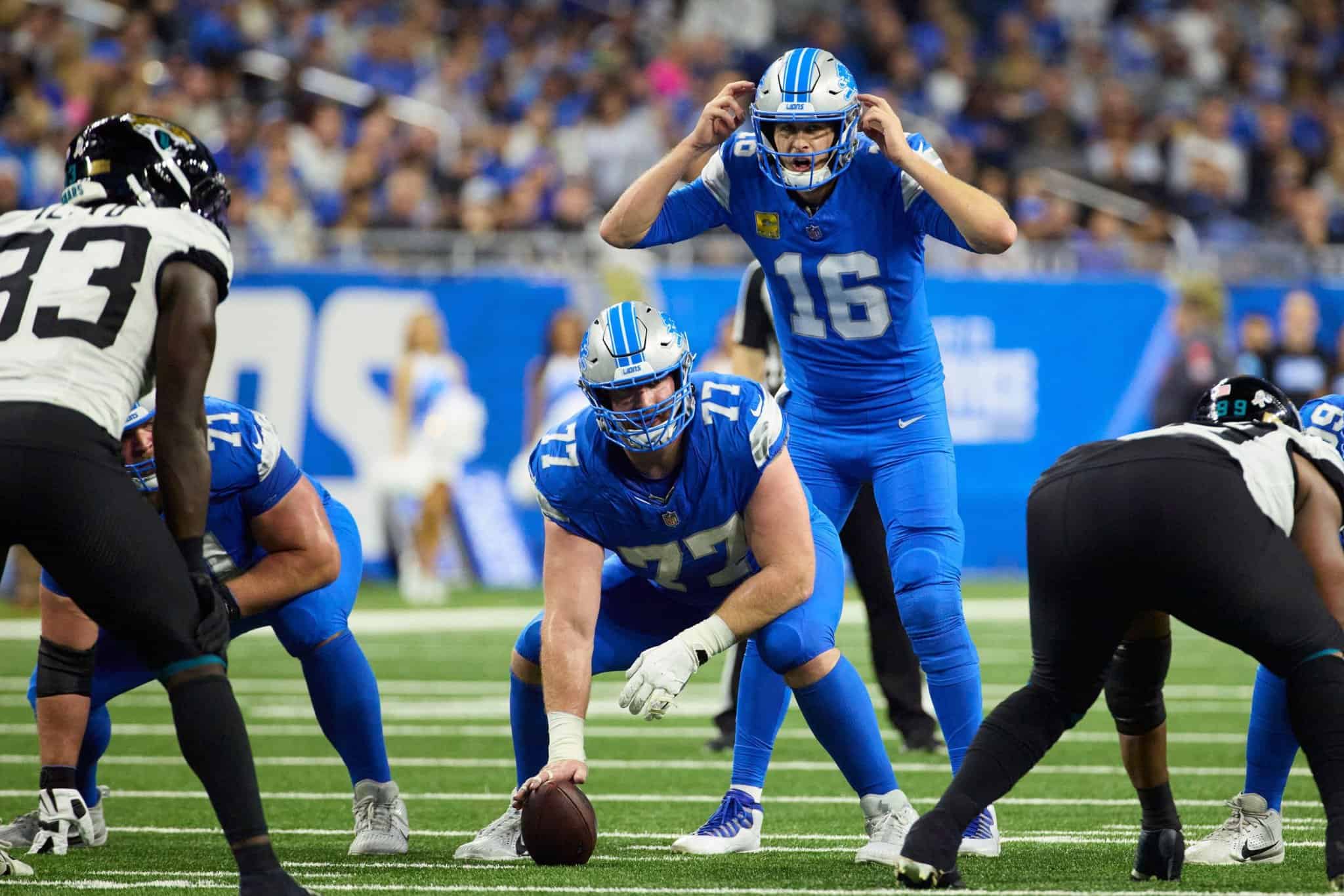 Downtown Detroit Lions quarterback scrambling during an NFL game against the Jacksonville Jaguars. Photo captures action on the field with players in blue uniforms, highlighting the intensity of professional football.