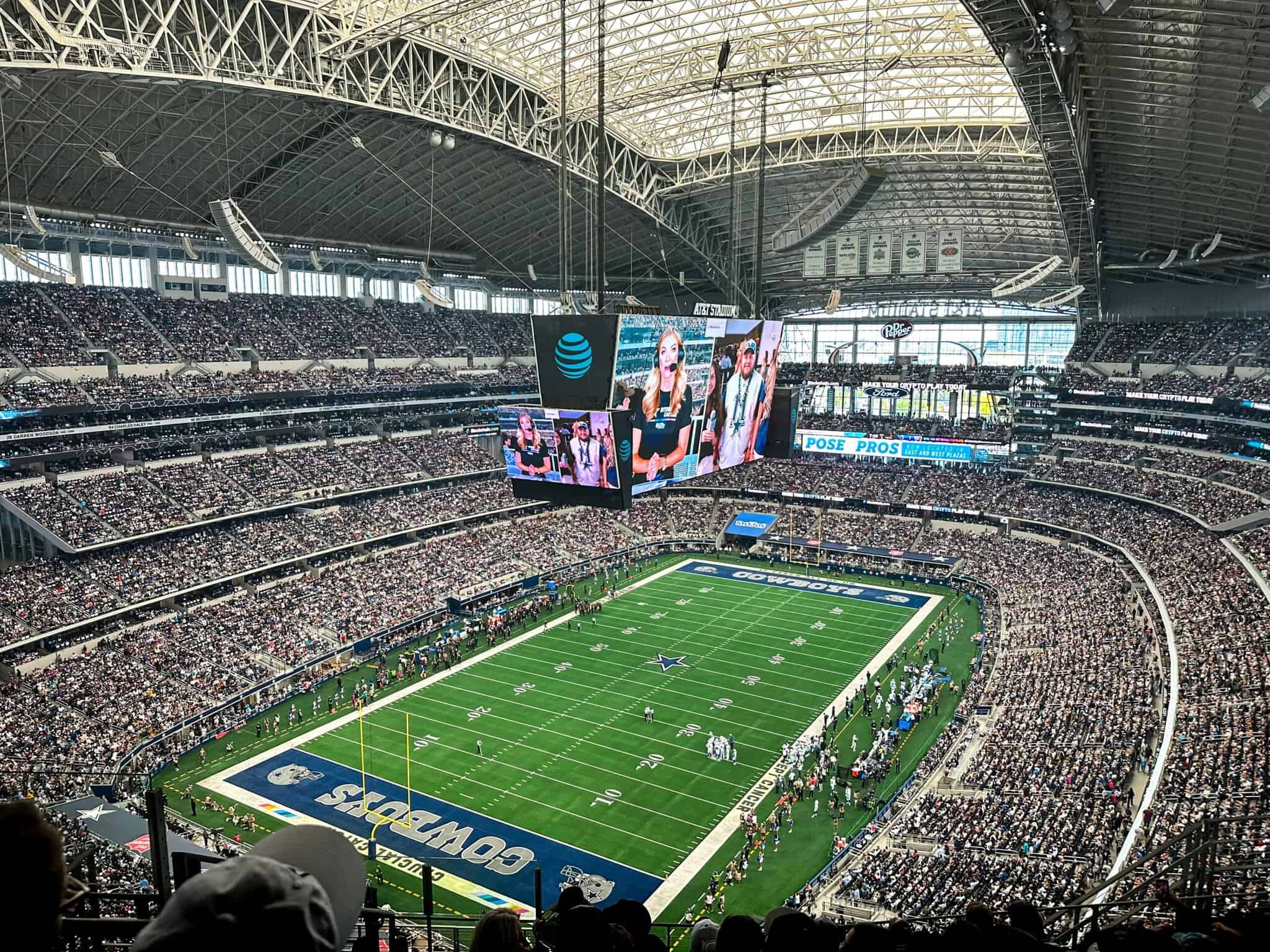 Jumbotron display showing commentators at AT&T Stadium during a Dallas Cowboys football game.