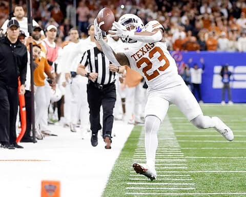 Caught in action, Texas Longhorns football player number 23 making a sideline catch during a game, surrounded by fans and referees on the field.